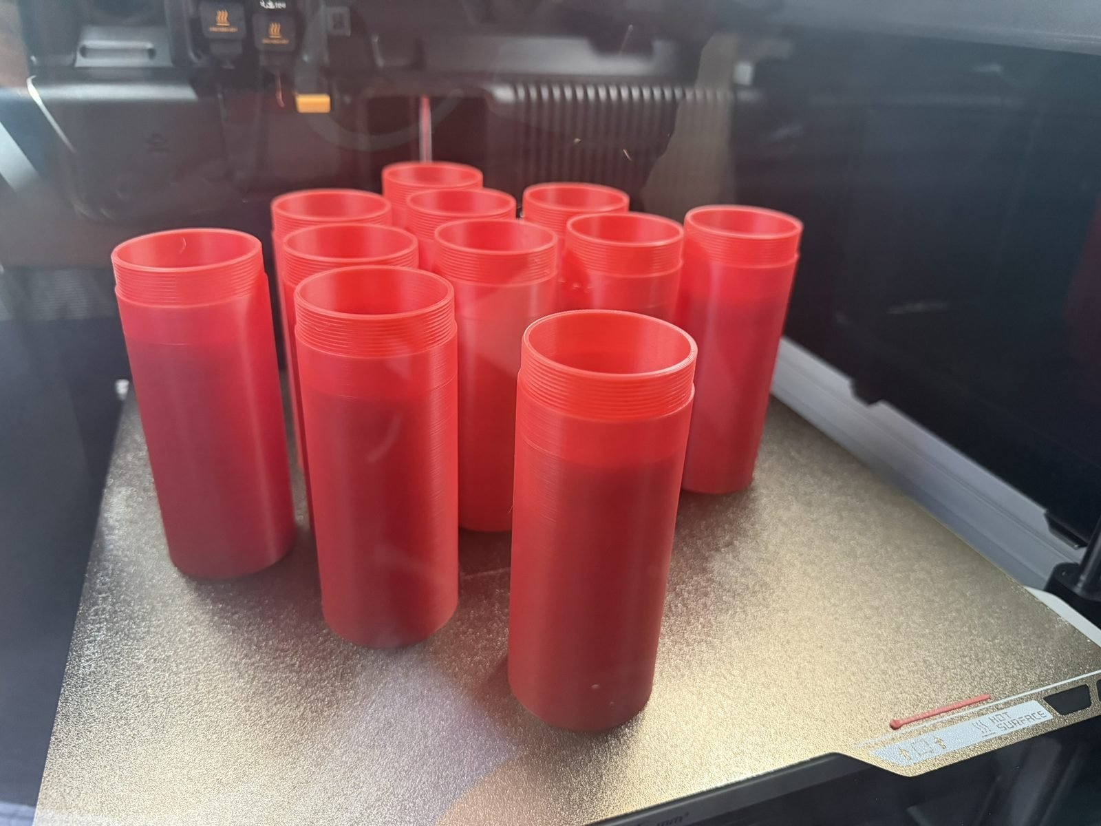 Batch of threaded red printed containers on the print bed